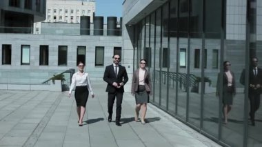 İş kıyafetleri ve güneş gözlükleriyle ofis binasının yakınlarında yürüyen üç iş adamı. Profesyonel insanlar kahve molasından dönüyorlar. İş konsepti. Prores 422