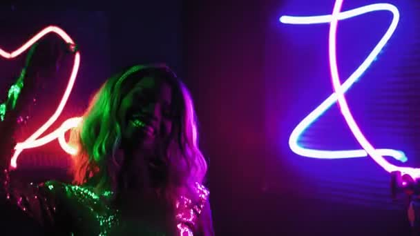 Saçlı mutlu Afro-Amerikalı sarışın kız siyah arka planda gümüş rengi bir pullu elbiseyle neon ışıklı ve makina dumanı içinde dans ediyor. Neon konsepti. Prores 422 — Stok video