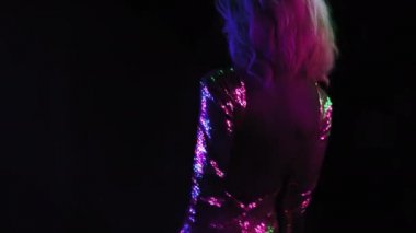 Gümüş pullu bir elbise giymiş Afrikalı bir kızın arkadan görünüşü müzik stüdyosu odasında siyah arka planda izole edilmiş neon renkli ışıkla dans ediyor. Neon konsepti. Prores 422