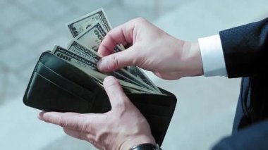 Soğuk tonda. İş adamının elleri, cüzdanı olan, takım elbiseli, dışarıda ofis binasının yanında oturan bir adamın elleri. Adam parayı saydı cüzdanı çantaya geri koydu. İş konsepti. Prores 422