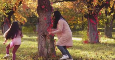 Anne, sonbahar parkında ağaçların arasında renkli bir peri masalı bahçesiyle kızın peşinde koşuyor. Tonlu görüntüler. Uzayı kopyala Aile kavramı. Prores 422
