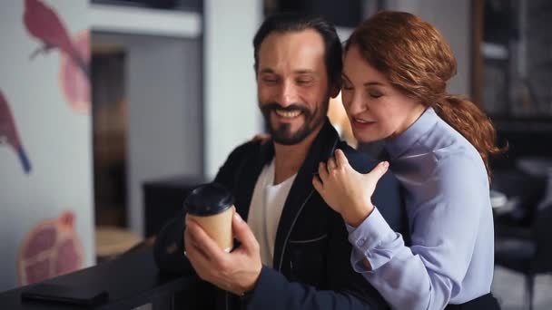 1 Mujer apoyada en los hombros del hombre leyendo el deseo impreso desde atrás hablando con el hombre y sonriendo En el amor pareja de personas de mediana edad de negocios sentados en una silla de un acogedor café. Imágenes tonificadas. Prores 422 — Vídeo de stock