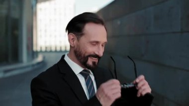 Soğuk tonda. İş adamı güneş gözlüğünü taktı açık havada, ofis binasının yanındaki güneşli sokakta duruyor. İş konsepti. Kapatın. Prores 422