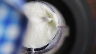 Blendere organik süt döküyorum. Koyu kahverengi ahşap bir masada duran mikserde hazırlanan milkshake. Süper yakın çekim. Prores 422