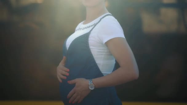 Mooie zwangere vrouw die op haar man wacht om haar op te pikken terwijl ze haar buik masseert terwijl ze naast de weg staat. Jonge vrouw met kort haar die een baby verwacht. Prores 422 — Stockvideo