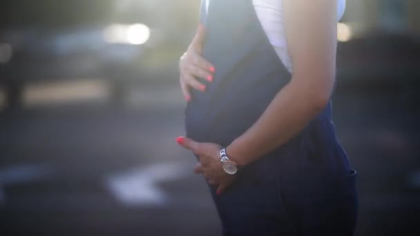 Fecha. Mulher grávida bonita em pé ao lado da estrada esperando o marido para buscá-la massageando sua barriga. Jovem com cabelo curto esperando um bebê. Prores 422 — Vídeo de Stock