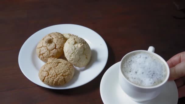 Mâinile femeii pun o ceașcă de cafea lângă prăjitura de pe placa albă care stă pe masa de lemn întunecată. Biscuiţi pe masă. Prores 422. Imagini FullHD de înaltă calitate — Videoclip de stoc