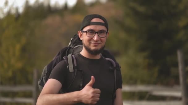 Um turista com óculos a mostrar o polegar a sorrir na câmara. Caminhante com uma grande mochila nas Montanhas Cárpatas. Movimento lento. Prores 422 — Vídeo de Stock