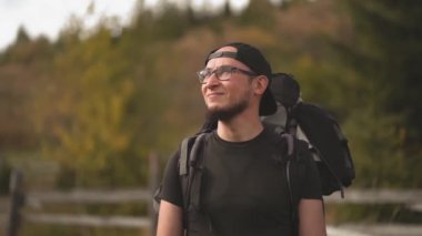 Gözlüklü yakışıklı sakallı turist elleriyle gözlerini kapatmak ve dağlara bakmak için elini kaldırıyor. Karpat Dağları 'nda büyük bir sırt çantalı bir yürüyüşçü. Ağır çekim. Prores 422