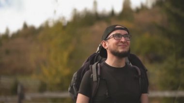 Gözlüklü yakışıklı sakallı turist kameraya gülümsüyor. Karpat Dağları 'nda büyük bir sırt çantalı bir yürüyüşçü. Ağır çekim. Prores 422