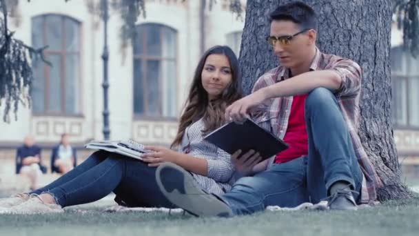 Deux étudiants, homme et fille, sont assis le dos appuyé sur un arbre et rêvent les yeux fermés. Un jeune couple d'étudiants passe du temps ensemble. concept d'éducation. Prores 422 — Video