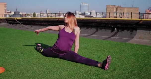 Fille brune sportive portant des vêtements de sport violets, faisant de l'exercice d'étirement de ficelle sur le toit avec un fond urbain. Prores 422 — Video