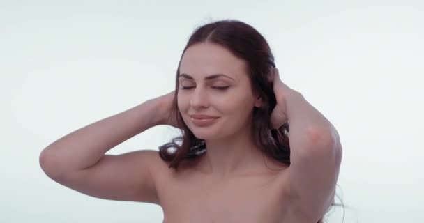 Jolie femme brune prenant soin des cheveux bruns en regardant la caméra, isolée sur fond blanc. Émotions filles avec un léger flirt. Concept de soins capillaires. Prores 422 — Video