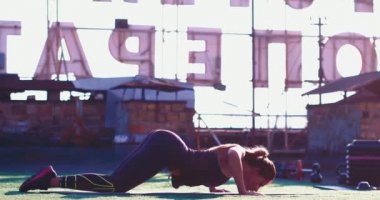 Binanın çatısındaki minderde yoga yapan kız. Sırtını kavisler ve öne doğru uzanıyor, sonra ilk yerine geri dönüyor..