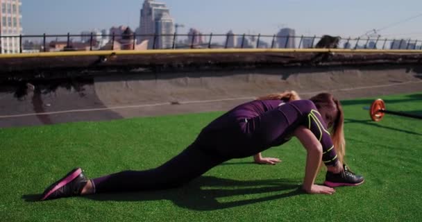 Athlète femme effectue un exercice sur l'étirement des jambes et des cuisses. La fille en position horizontale a jeté une jambe sur le bras. La deuxième jambe est en retrait. Matin Kiev en arrière-plan. — Video