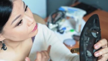 Kadın kendi makyajını yaptı ve aynaya baktı. Gölgelerin kalıntılarını ovuşturuyor. Makyaj kendi el konseptinle yapılır. Yüksek kalite 4k görüntü