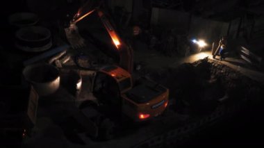 Kazı makinesi gece yırtılıyor. Kovayı çukura çeviriyor. Karanlıkta inşaatçıların ve inşaat alanlarının arka planına karşı. Yüksek kalite 4K görüntü. 26 Haziran 2020. Kyiv, Ukrayna