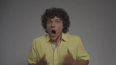 Kıvırcık saçlı adam şoka giriyor. Stüdyodaki genç adam izole bir arka planda şaşkınlık ve şoku resmediyor. Yüksek kaliteli FullHD görüntüler
