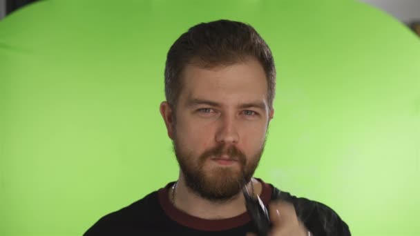 Een man met een baard rookt een e-sigaret in de studio op een geïsoleerde achtergrond. Het geeft damp uit de mond en neus vrij. Hoge kwaliteit 4k beeldmateriaal — Stockvideo