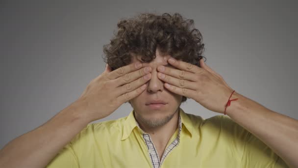 Young curly-haired guy writhes his faces on camera. He closes his eyes with his palms and lifts the corners of his lips up. High quality 4k footage — Stock Video