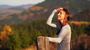 Bir dağ kadınının önünde duran kadın çitin üzerinde oturur ve dağ manzarasına hayran kalır. Saçını düzleştirir ve elini kaldırır. Arkaplanda dağ manzarası. 