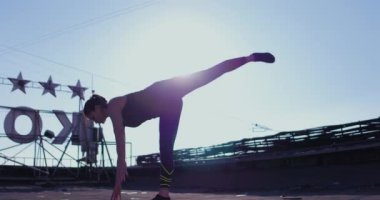 Kadın dışarıda askıda geriniyor. Bir bacağını kaldırıyor ve dengesini koruyor.