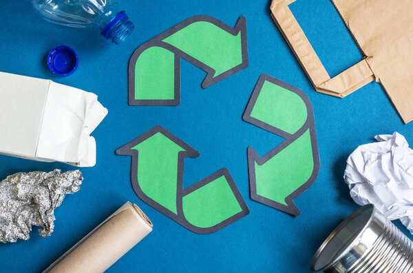 Concept of household waste recycling: various wastes and a recycling sign on a blue background. Top view, close-up