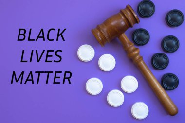Black and white checkers lie on a purple background, separated by a judge's hammer. The inscription BLACK LIVES MATTER. The concept of combating discrimination and racism. Close-up, top view