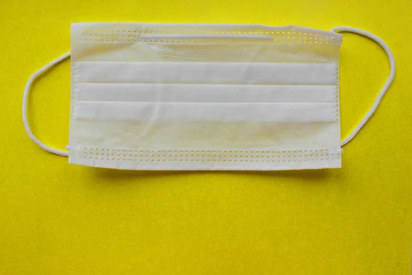A medical mask to protect against viruses. A disposable mask. On a yellow background. A white mask. Medicine. Virus protection. Background. The mask is located from top to middle. Copy space. — Stock Photo, Image