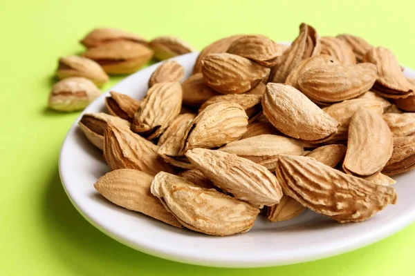 Bademler beyaz bir tabakta soyulmaz. Sarı arka plan. Yukarıdan bak. Atıştırmak için kavrulmuş badem. Kaçık. Yiyecekler. Açlığı bastırıyor. Protein. Kabuklu fındıklar. Boşluğu kopyala