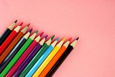 Pembe arka planda renkli kalemler. Bir sürü farklı renkli kalem. Renkli kalem. Kalemler keskindir. Kalemler sol alt köşede çaprazlama duruyor. Yakın plan. Uzayı kopyala Geçmişi. Düz yatıyordu.