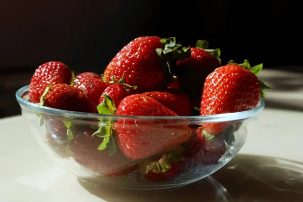 Fraises fraîches mûres délicieuses dans une assiette en verre sur la table.Pile de fraises rouges sur une assiette close-up. De la nourriture. Des vitamines. Ferme. Espace de copie pour le texte — Photo