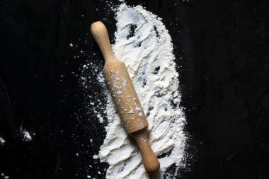 Un kaplı siyah bir yüzeyde hamuru yuvarlamak için merdane. Merkezde yer alıyor. Yukarıdan manzara. Pişirme. Ev yapımı yemek. Metin için alanı kopyala