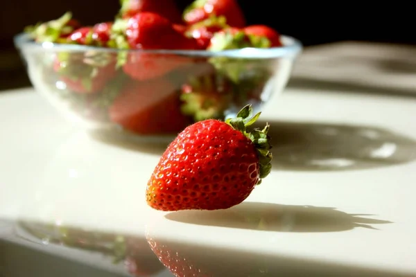 Verse rijpe heerlijke aardbeien in een glazen bord op tafel. Borst van rode aardbeien op een bord close-up. Een aardbei ligt ernaast. Kopieerruimte voor tekst — Stockfoto