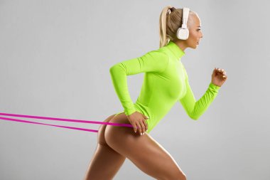 Fitness kadın onun egzersiz bir direnç bandı kullanarak. Gri arka planda Expander ile seksi atletik kız egzersiz. Bronzlaşmış deri ile güzel popo