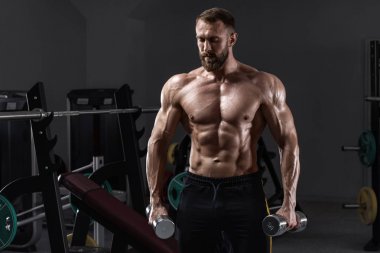 Jimnastik salonunda dambıllı kaslı bir adam. Güçlü erkek çıplak gövde abs, egzersiz