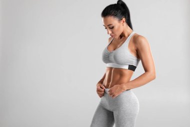 Fitness kadın abs ve düz karın gösteren, gri arka plan üzerinde izole. Güzel atletik kız, şekilli karın
