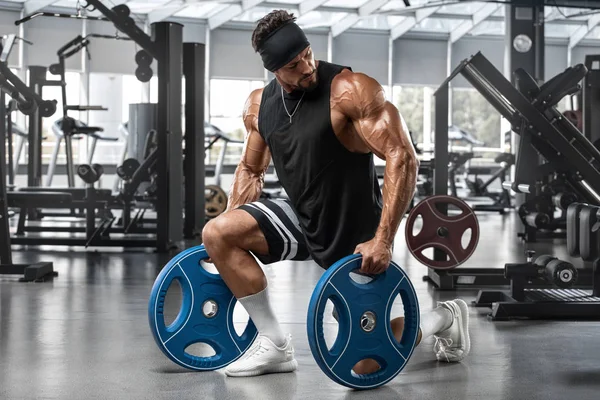 Spor salonunda kaslı adam egzersiz. Güçlü erkek gösteren kaslar