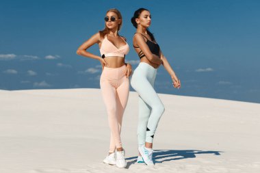 Beautiful fitness models in sportswear. Couple athletic girls in leggings outdoor clipart