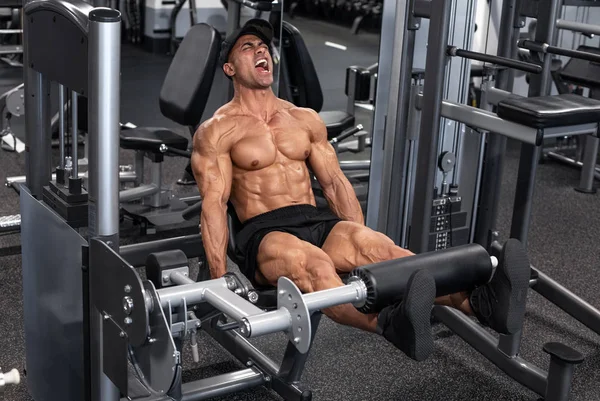 Spor salonunda bacak egzersizi yapan kaslı adam, güçlü erkek kuadriseps egzersizi.