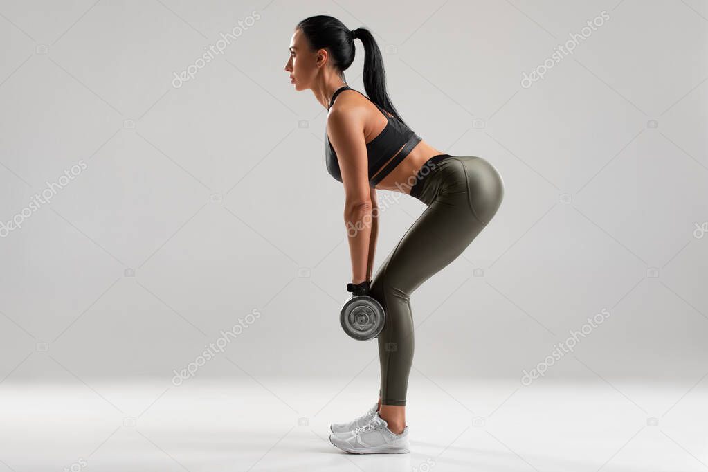 Fitness woman doing exercise for glutes on gray background. Athletic girl workout with dumbbells