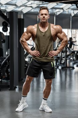 Muscular man showing muscles in gym. Strong male bodybuilder