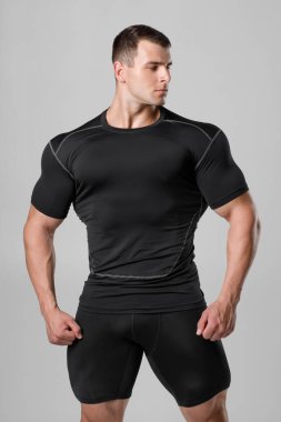 Gri arka planda siyah sıkıştırmalı spor giyimli kaslı adam.