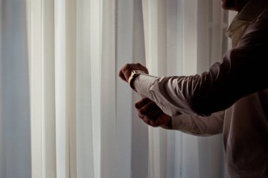 Penceredeki beyaz gömlekli adam altın bir saat takıyor.