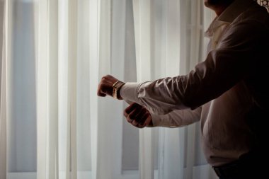 Penceredeki beyaz gömlekli adam altın bir saat takıyor.