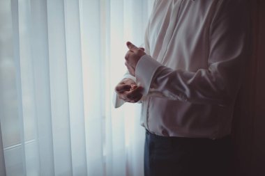 Pencere kenarındaki beyaz gömlekli adam. Kol düğmeleri.