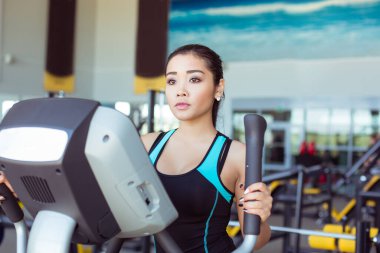 Çekici Asyalı kız jimnastik salonunda XTrainer makinesinde egzersiz yapıyor.