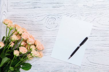 Beyaz kart, kalem ve ahşap arka planda pembe güller.