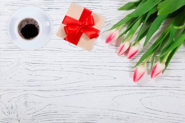 Ahşap arka planda lalelerin yanında bir fincan kahve ve hediye kutusu.