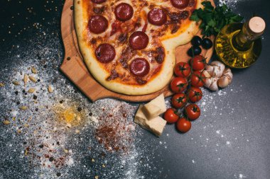 Pepperoni, domates, mozzarella, sarımsak ve siyah arka planda maydanoz şeklinde pizza kalbi.
